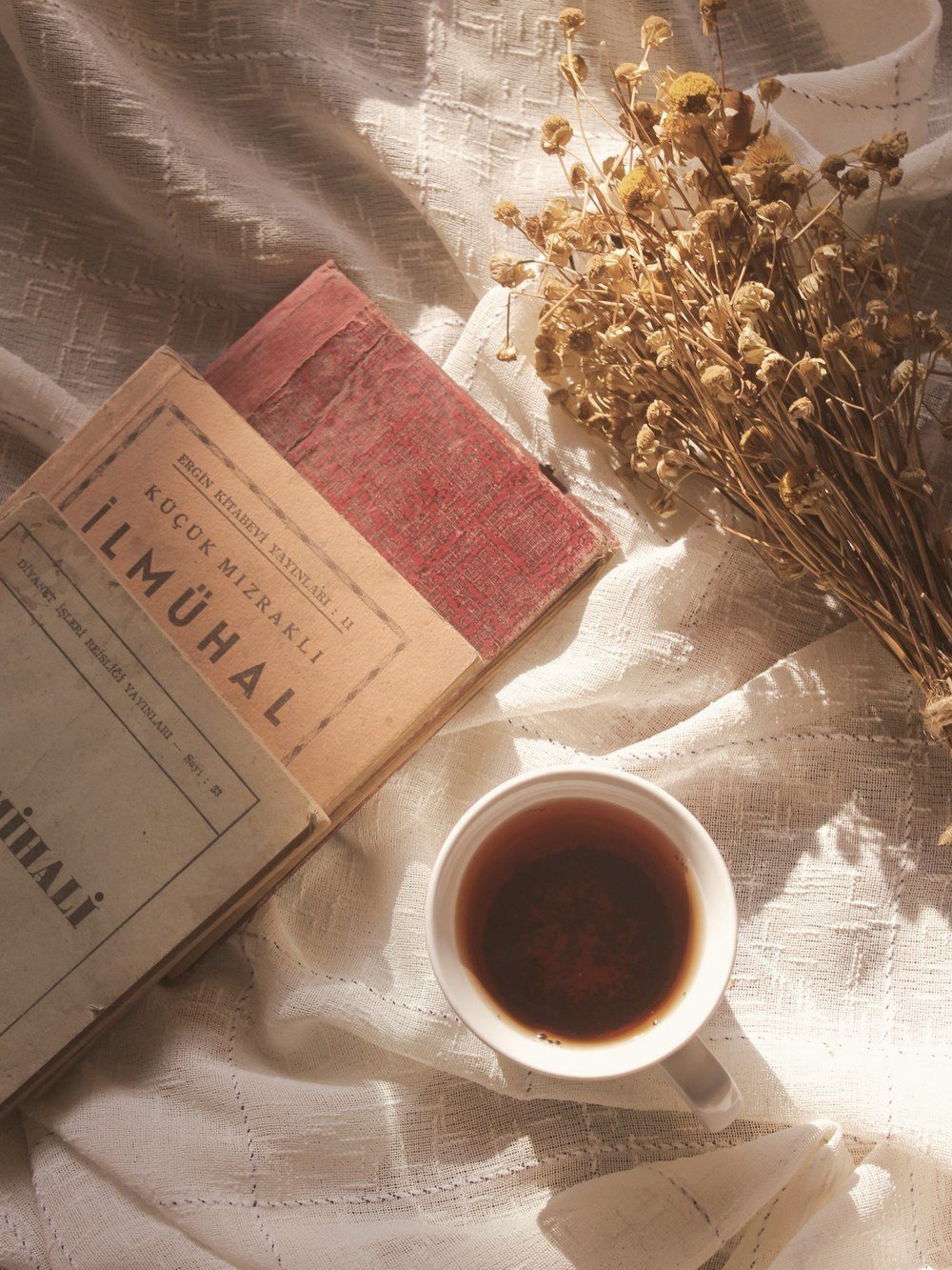 A cup of herbal tea beside dried flowers and books